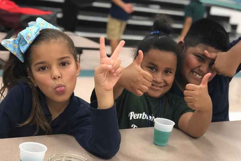 Three children making hand gestures at a table