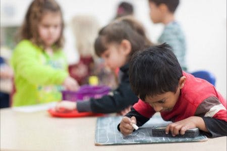 Child writing on a chalkboard with other children in the background