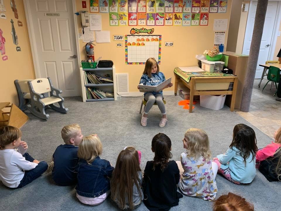 Child reading a book to other children in a classroom