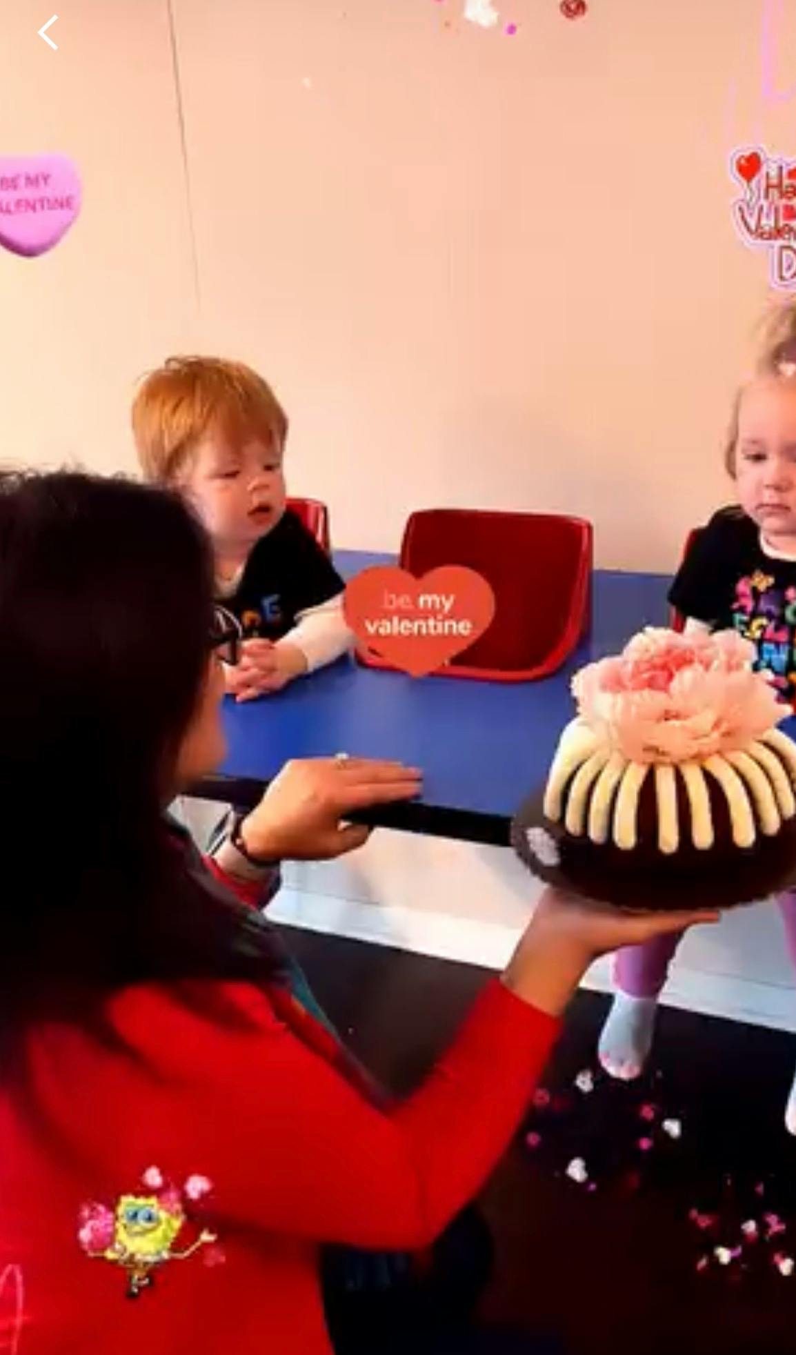 Person holding a bundt cake toward two children sitting at a table
