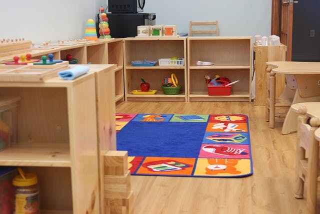 Classroom with wooden shelves, colorful rug, and small tables