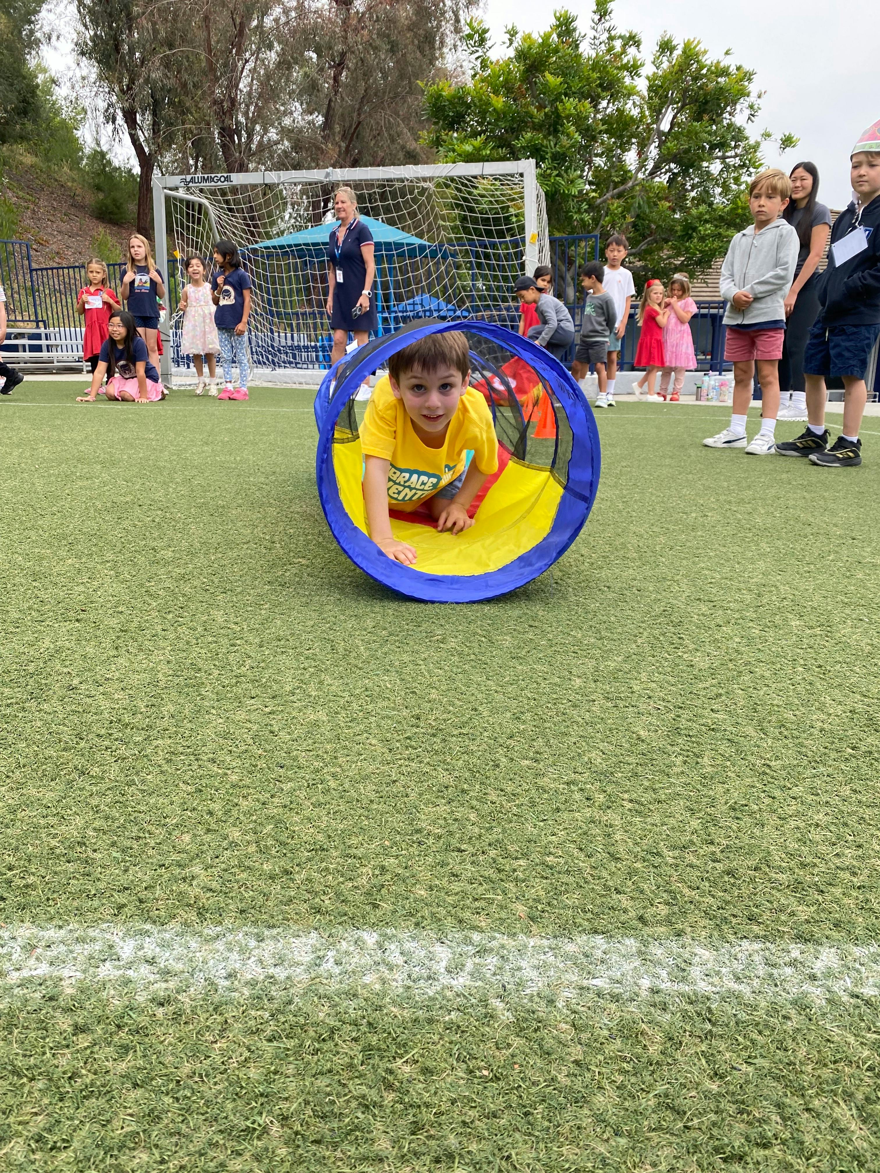 Child crawling through a blue and yellow tunnel on a grassy field