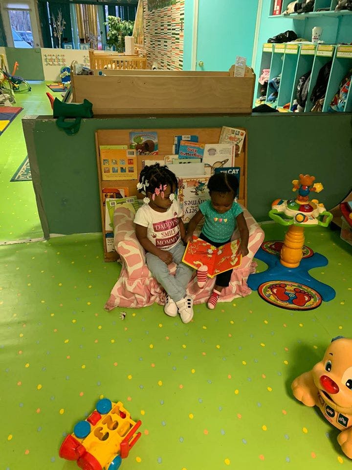 Two children sitting on a small couch, one holding an open book