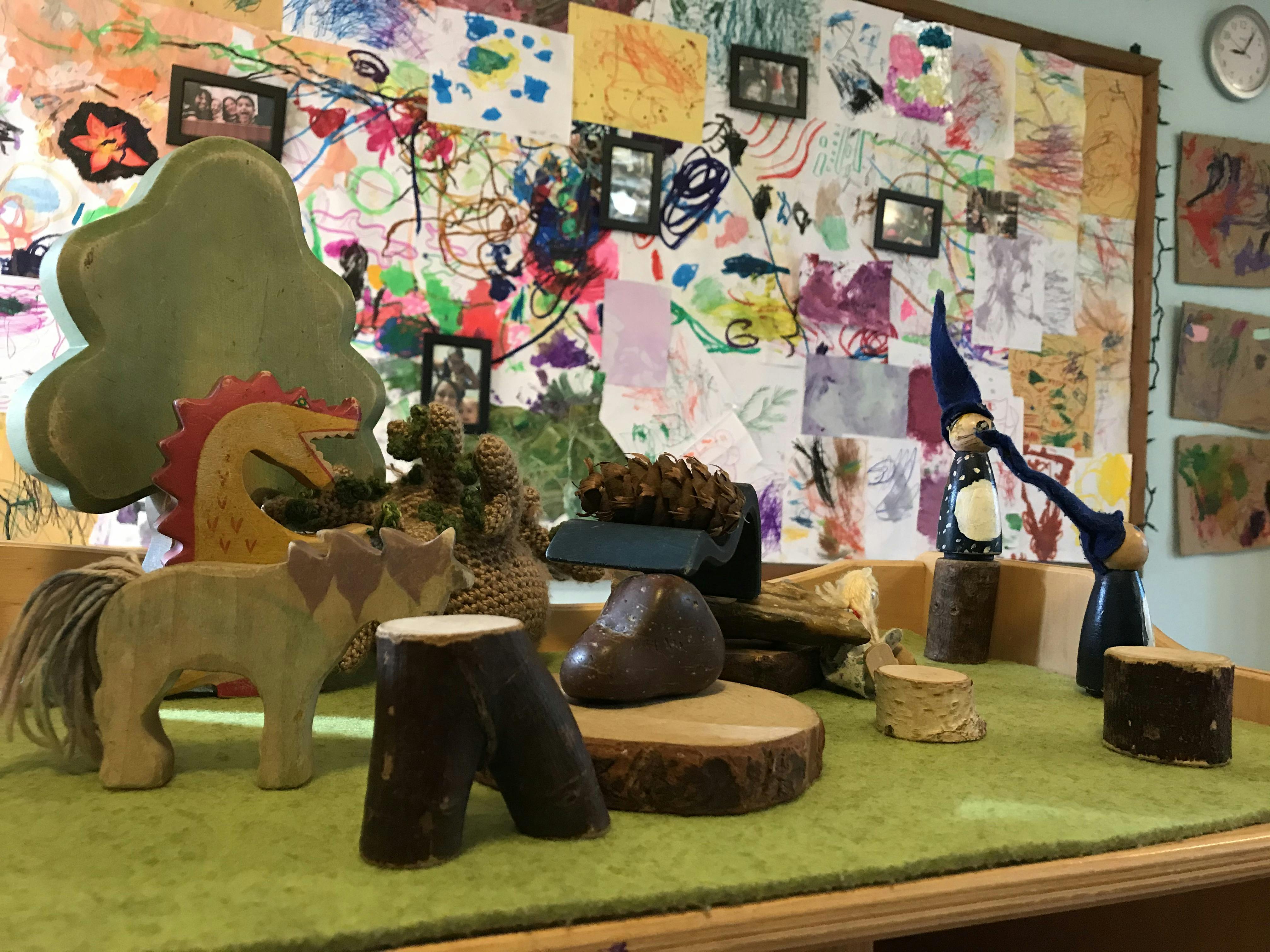 Wooden toys and natural elements on a green surface in front of children's artwork