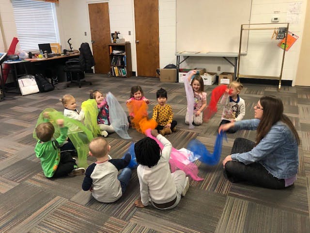 Adult and children sitting on floor playing with colorful scarves