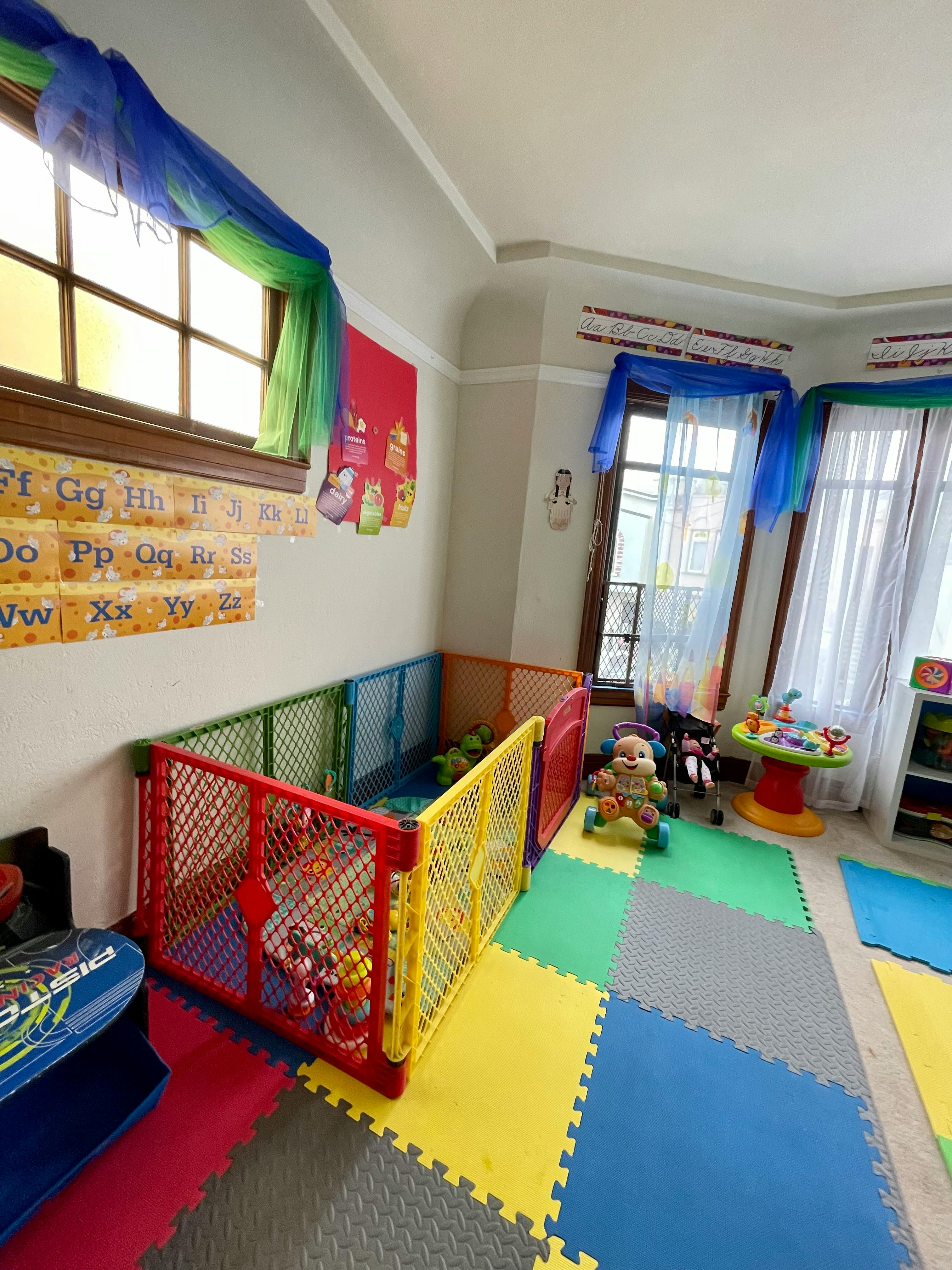 Playroom with colorful floor mats, a playpen, and windows with blue and green drapes