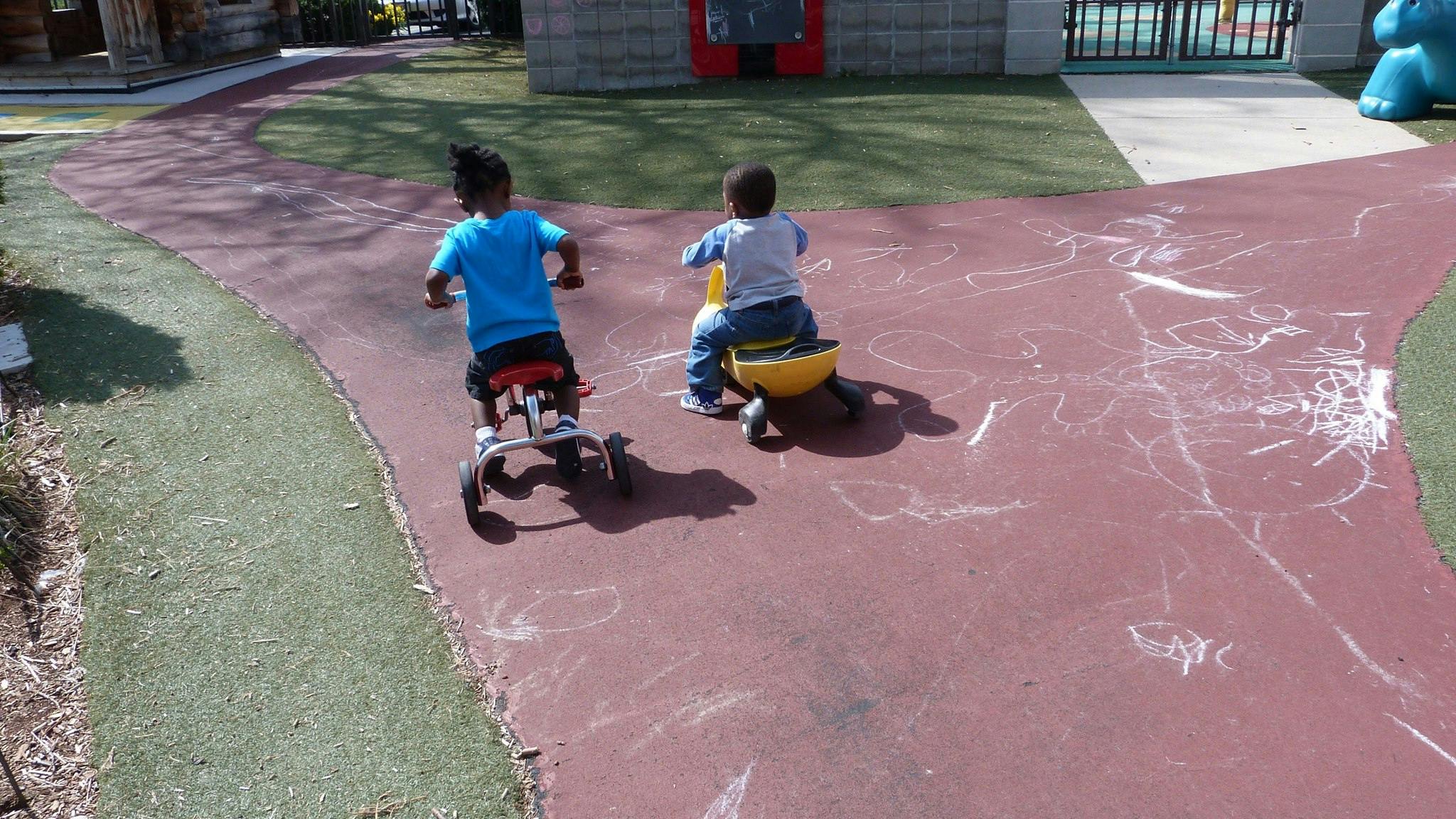 Two children riding tricycles on a paved path
