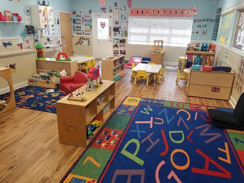 A colorful classroom with small tables, chairs, and an alphabet rug