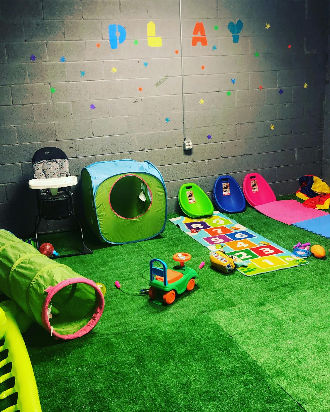 Indoor play area with green turf, play tunnel, tent, and ride-on toy