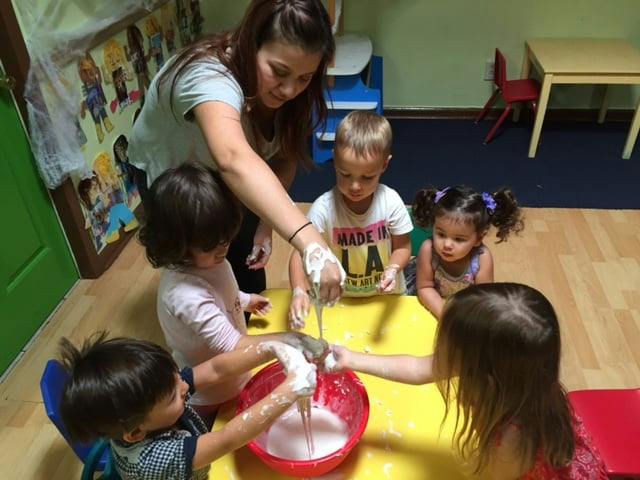 Person and children playing with slime in a red bowl