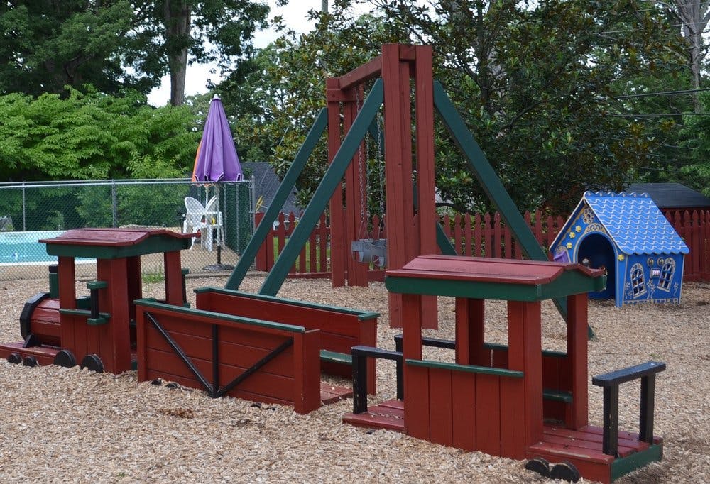 Wooden train playground structure with a swing set and small blue playhouse