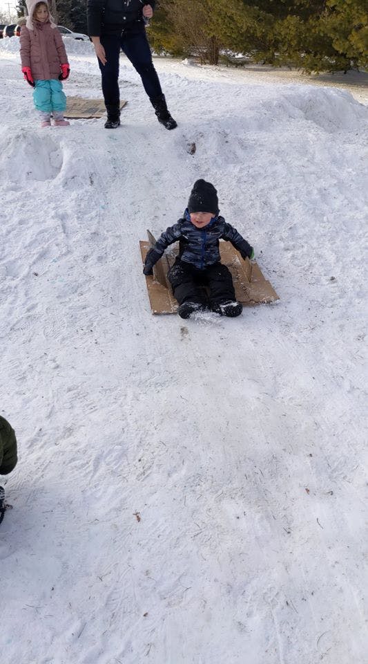 Child sledding down a snowy hill on a piece of cardboard