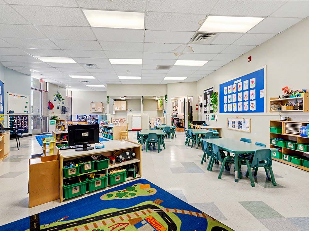Classroom with small green tables and chairs, and a blue rug with a road design