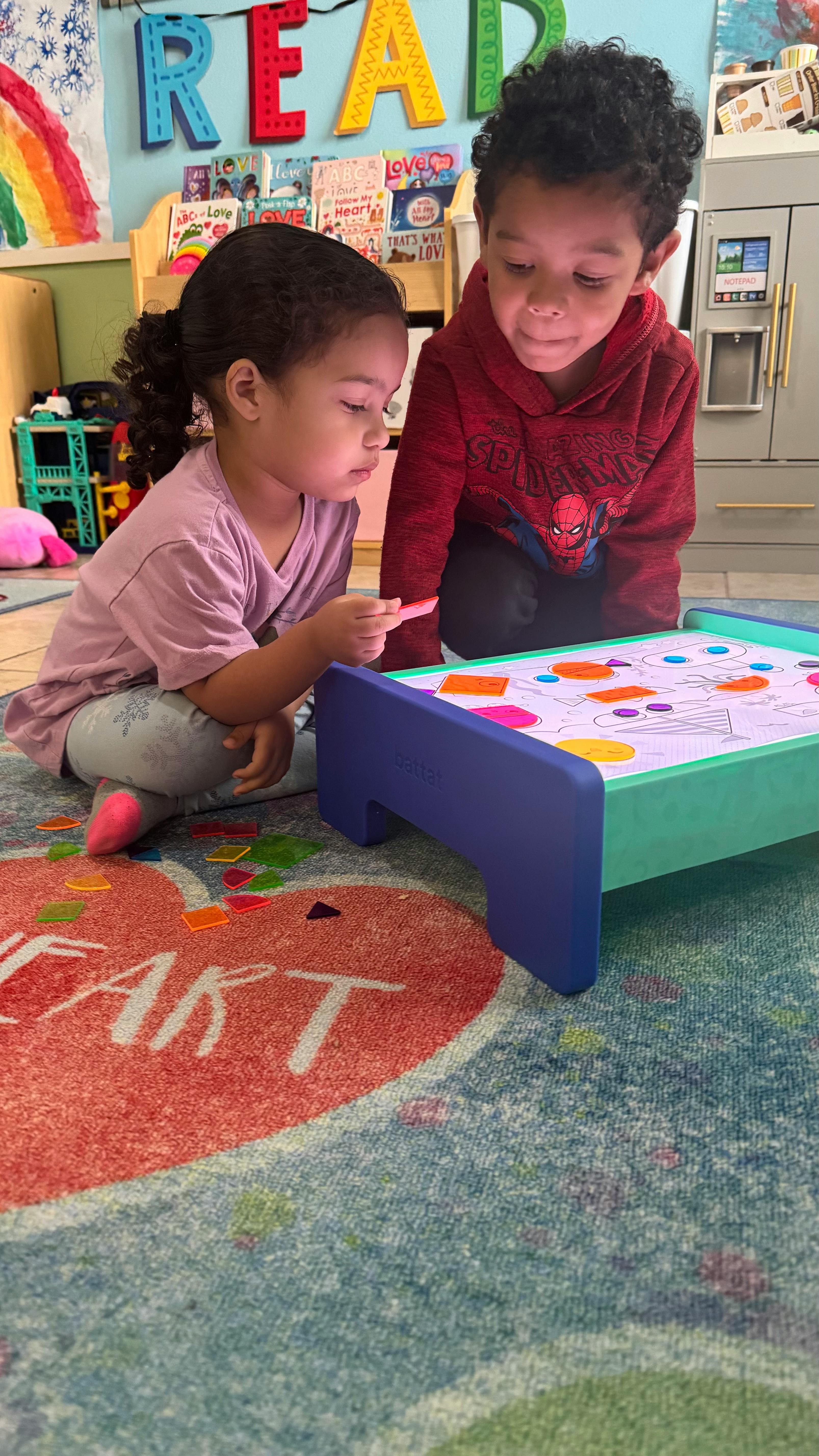 Two children playing with a light-up activity board on the floor