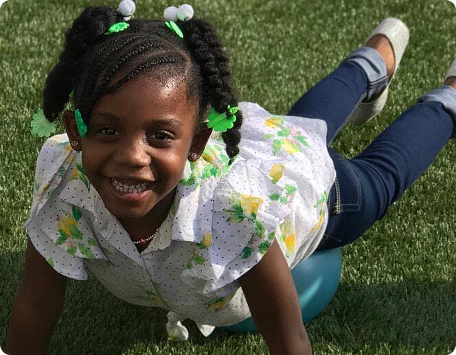 Child lying on stomach on a blue ball on grass
