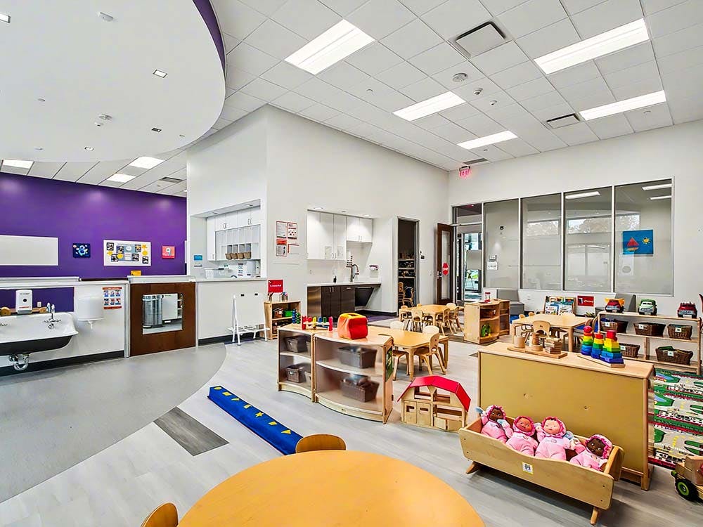 A colorful classroom with play tables, child-sized furniture, and play kitchens