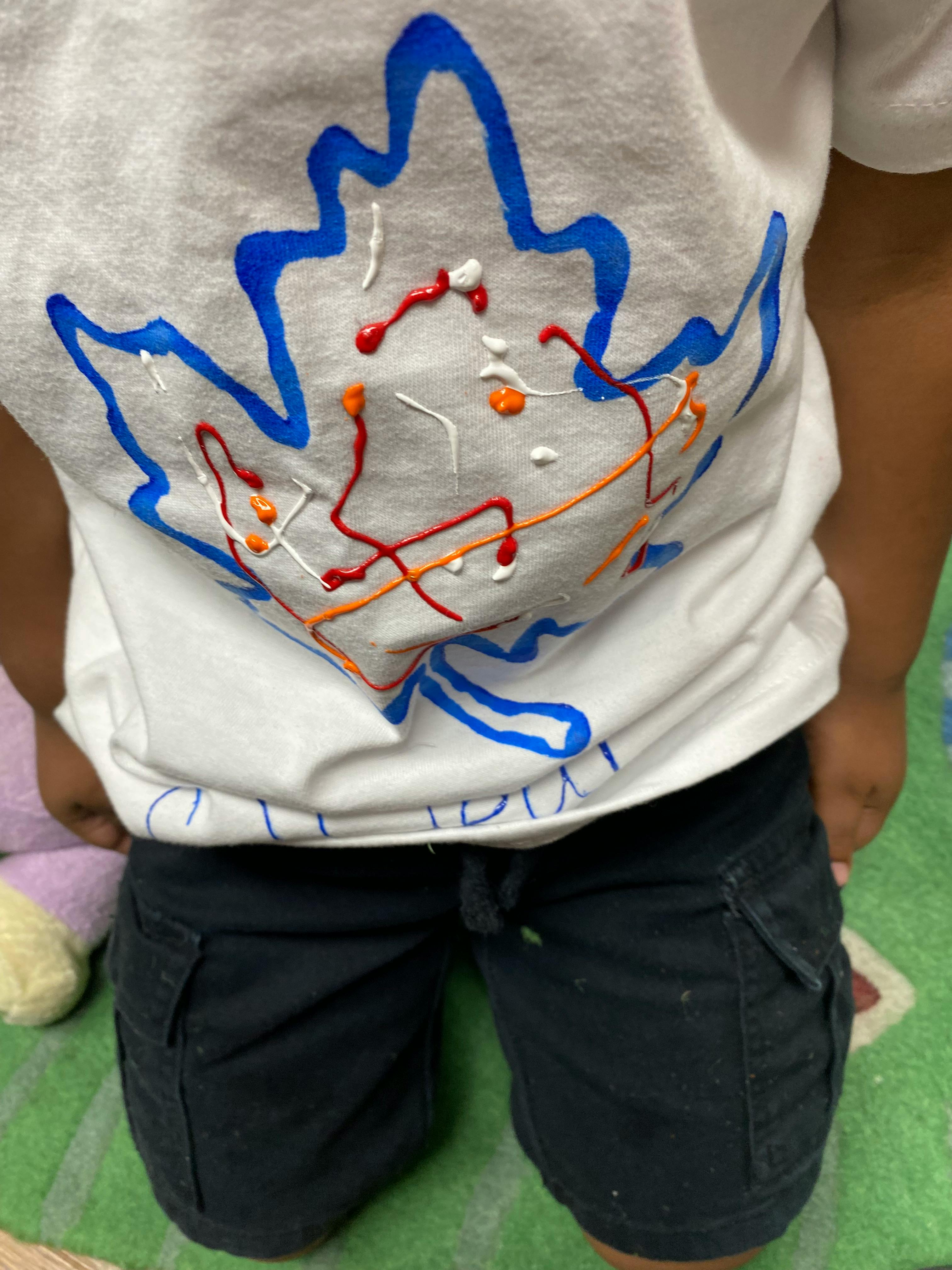 Child wearing a white shirt with a blue maple leaf design and paint splatters
