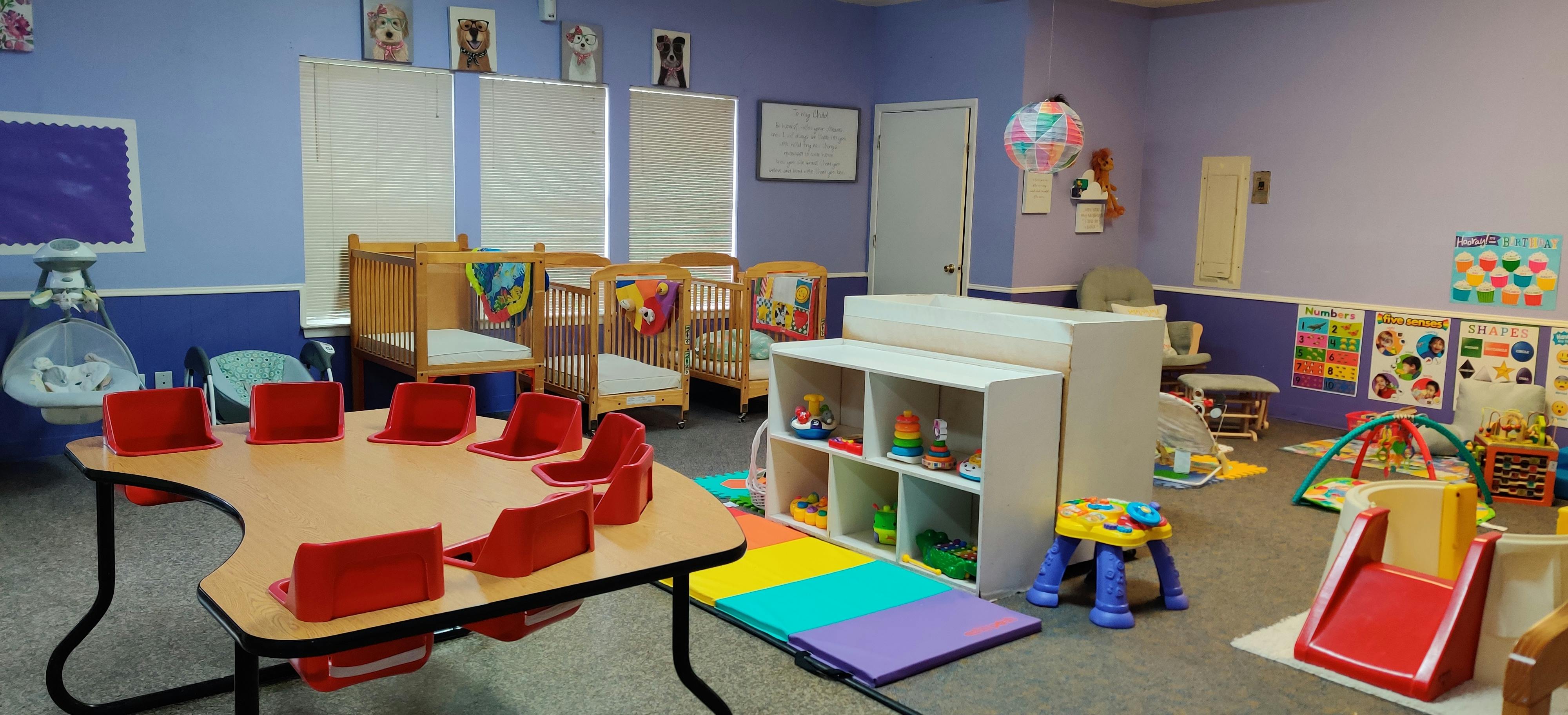 Classroom with small tables, cribs, and play equipment