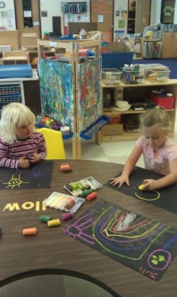 Two children drawing with chalk at a table in a classroom