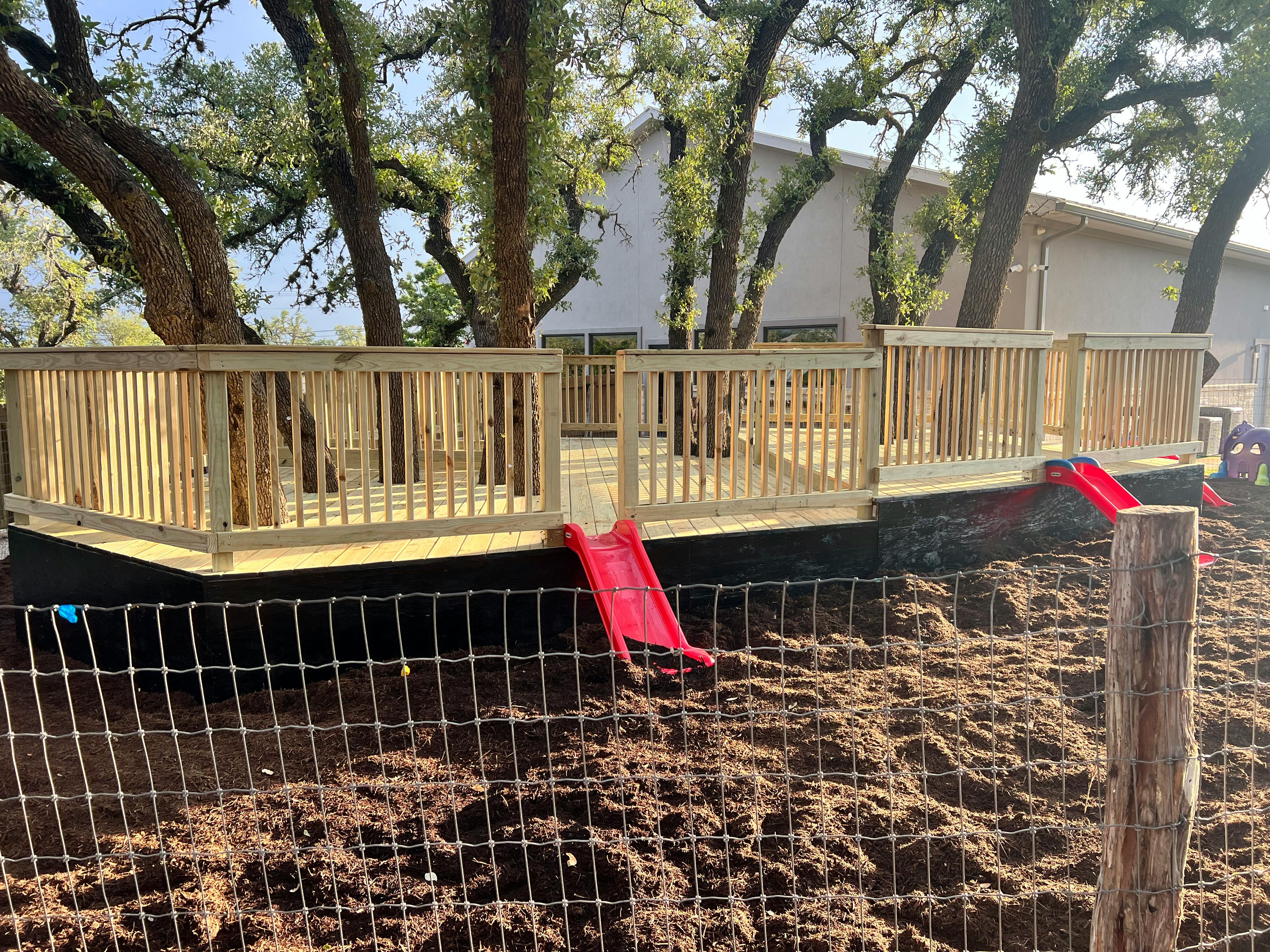 Wooden deck with railings and two red slides leading to the ground