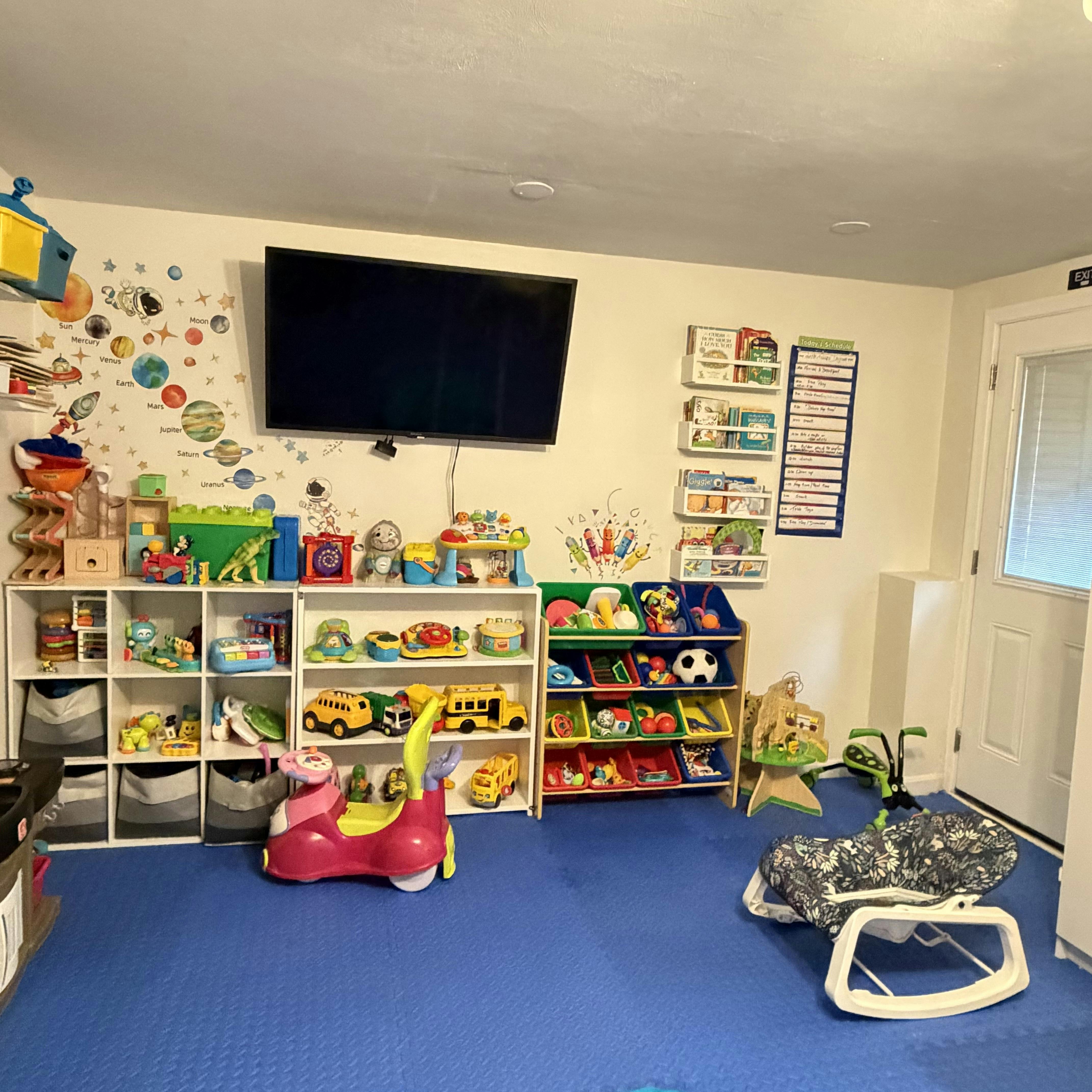 A playroom with organized toys, a television, and a solar system wall decal