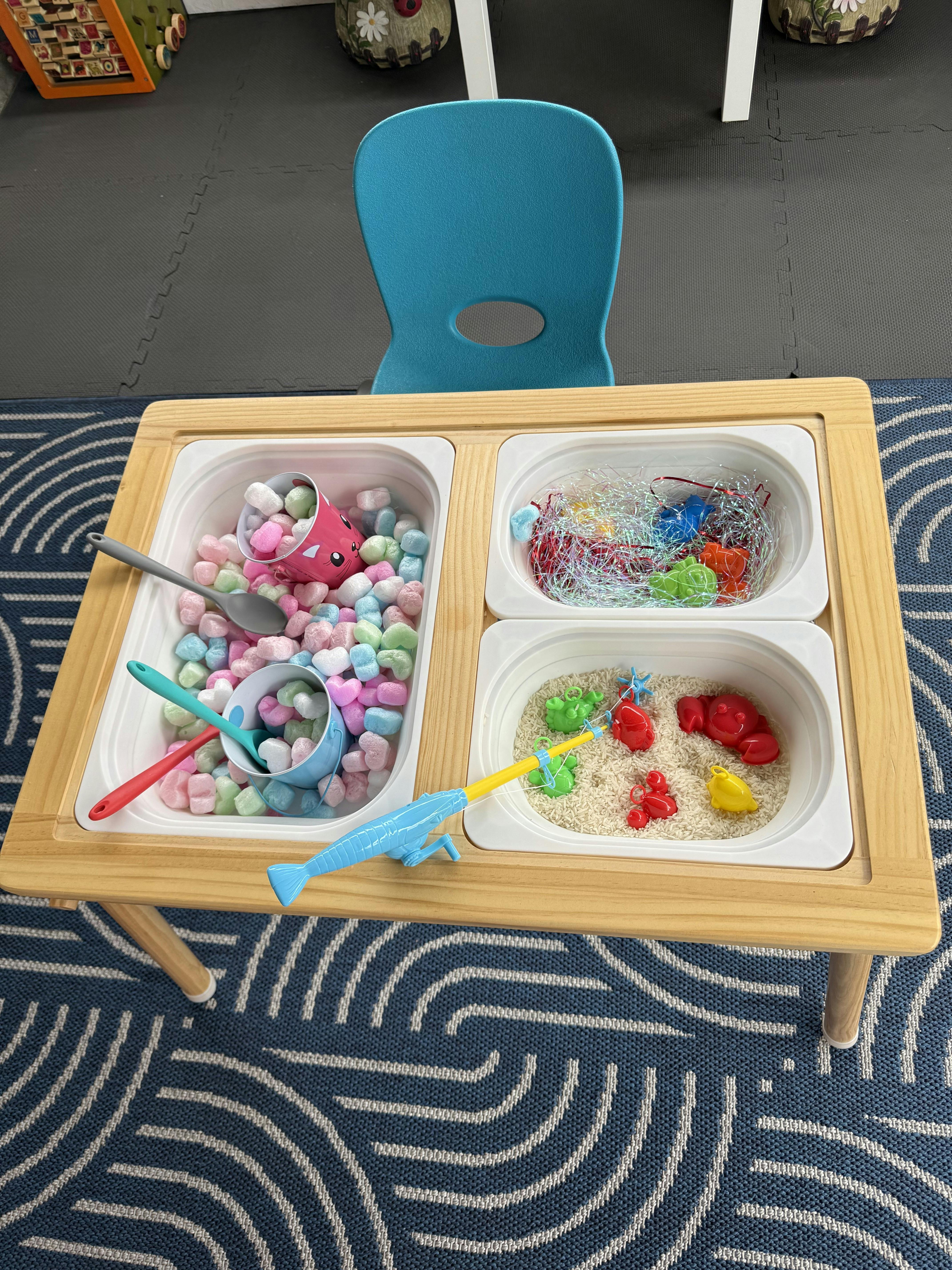 Sensory table with bins of colorful objects and rice with a fishing toy