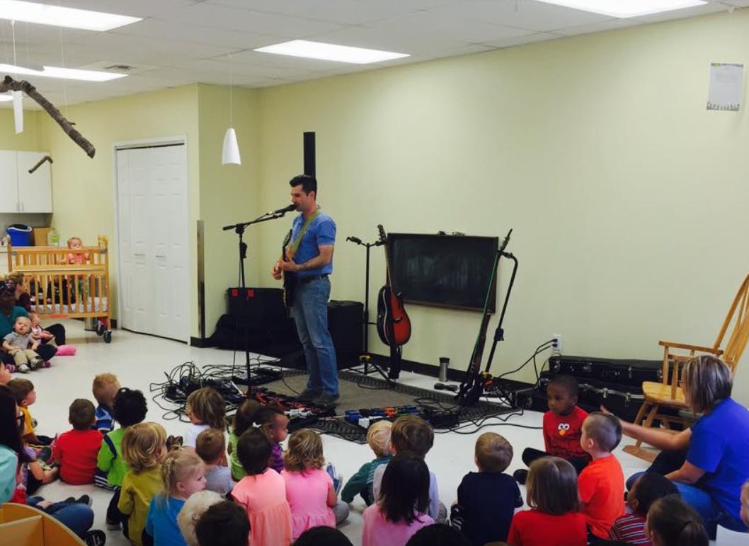 Person playing guitar for a group of children sitting on the floor