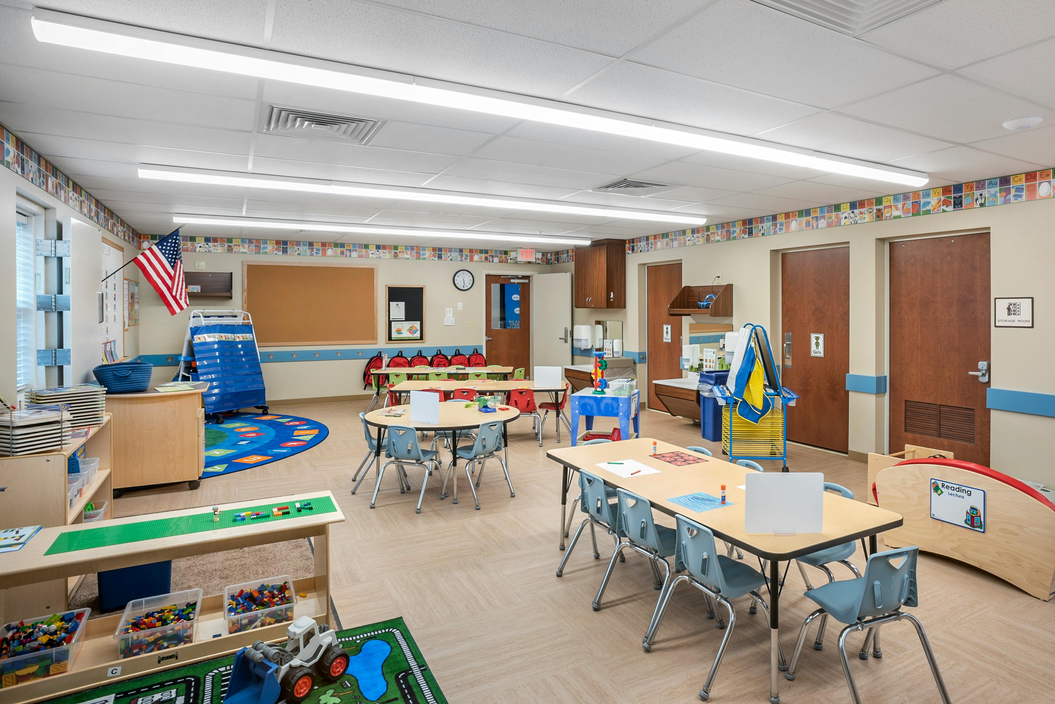 Classroom with small tables and chairs, a play rug, storage, and sinks