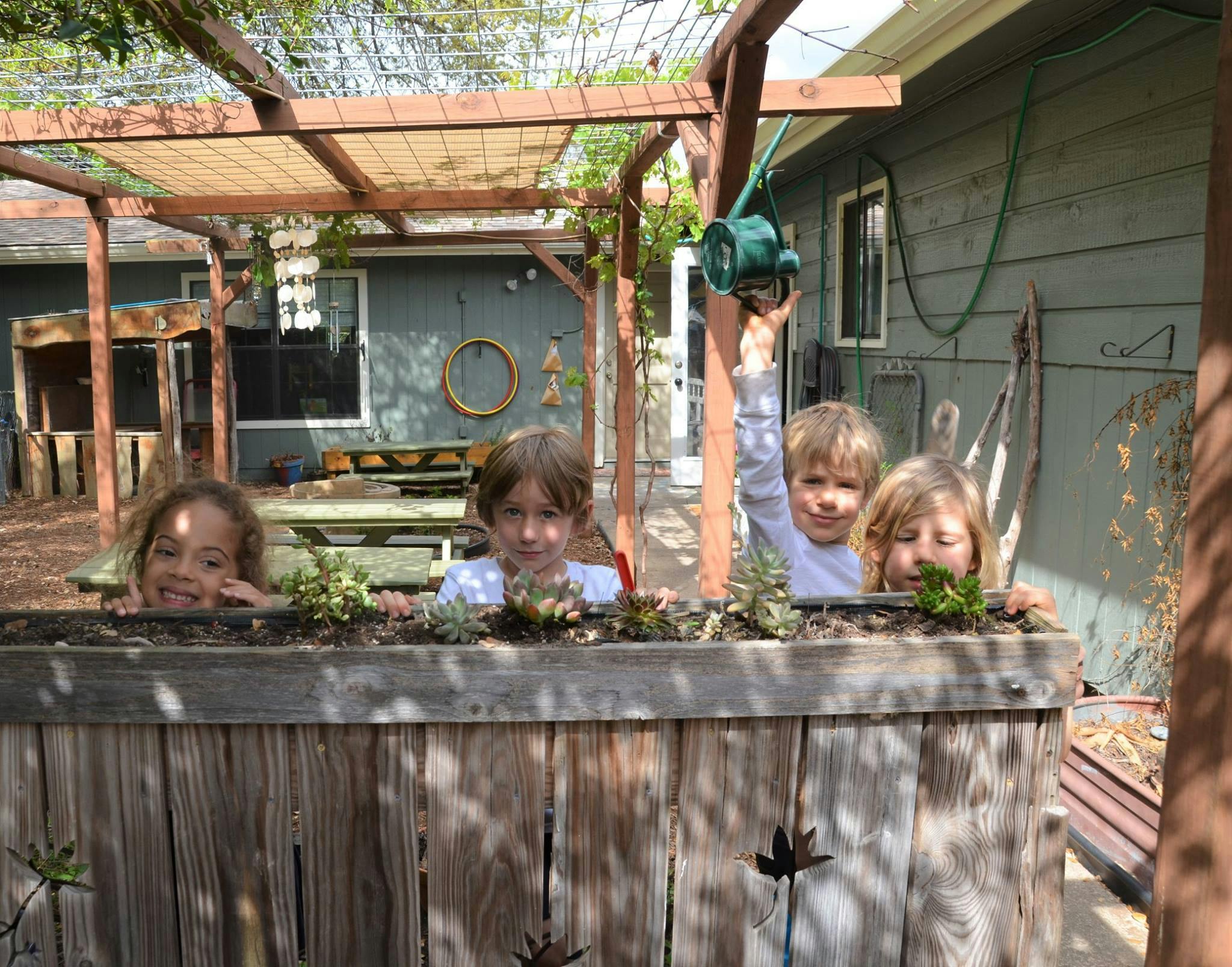Four children looking over a wooden planter