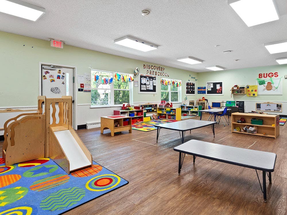 A colorful classroom with tables, chairs, and a small play slide