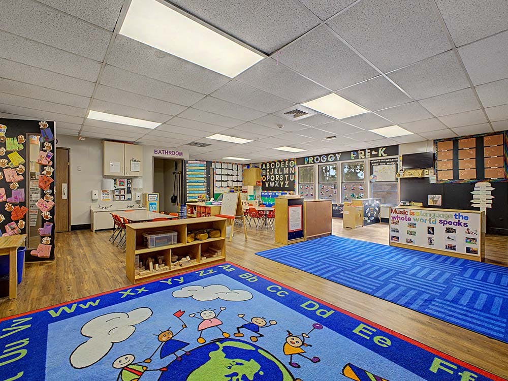 Classroom with children's rugs, small tables and chairs, and various learning displays