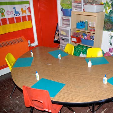 Classroom table with chairs, paper, and glue bottles