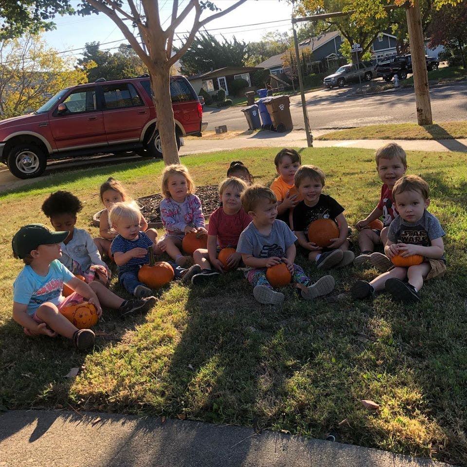 Group of children sitting on grass holding small pumpkins