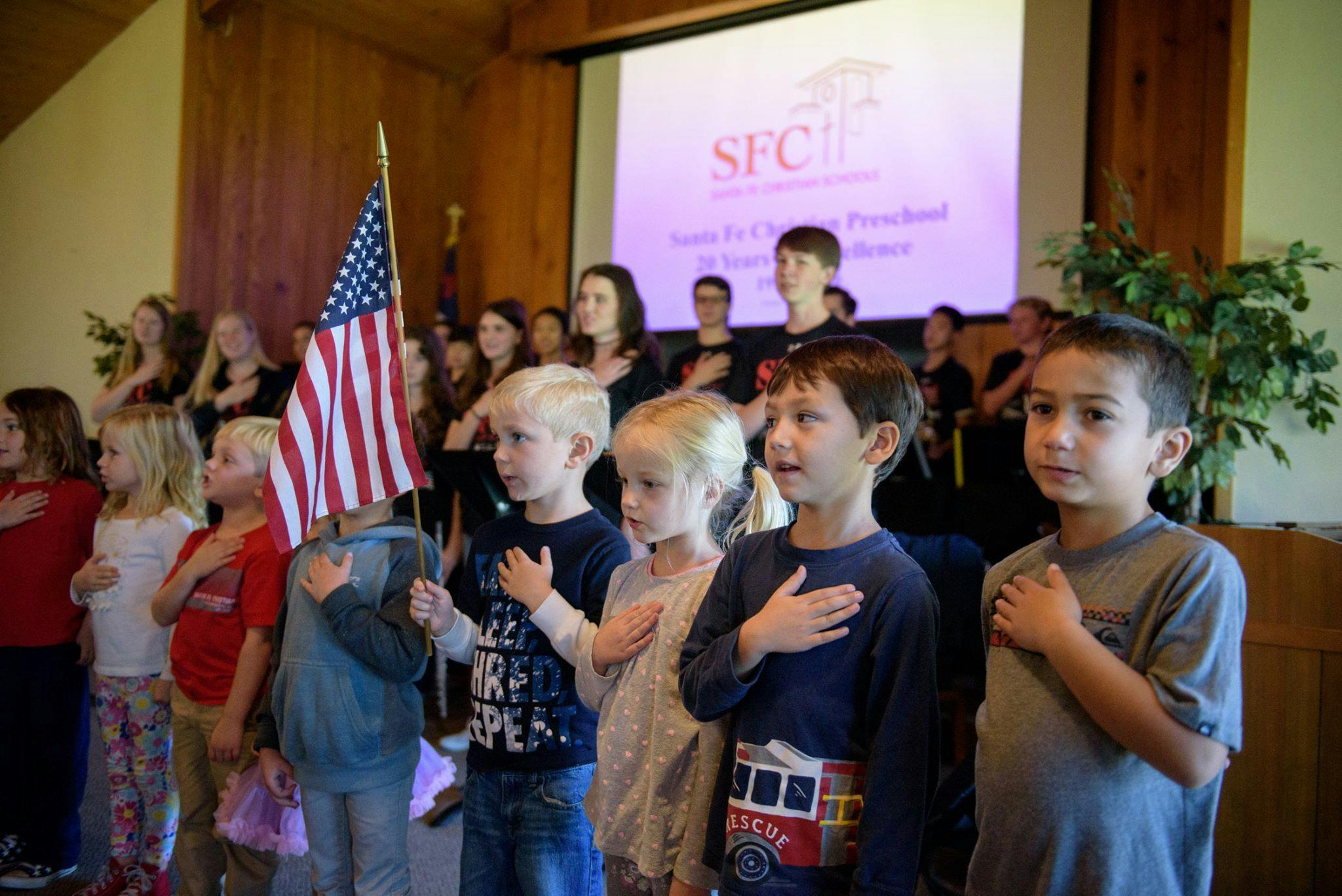 Children and adults standing with hands over hearts, American flag visible