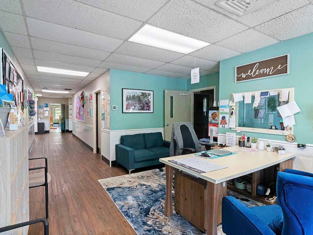 An office reception area with a desk, two blue chairs, a turquoise couch, and a long hallway