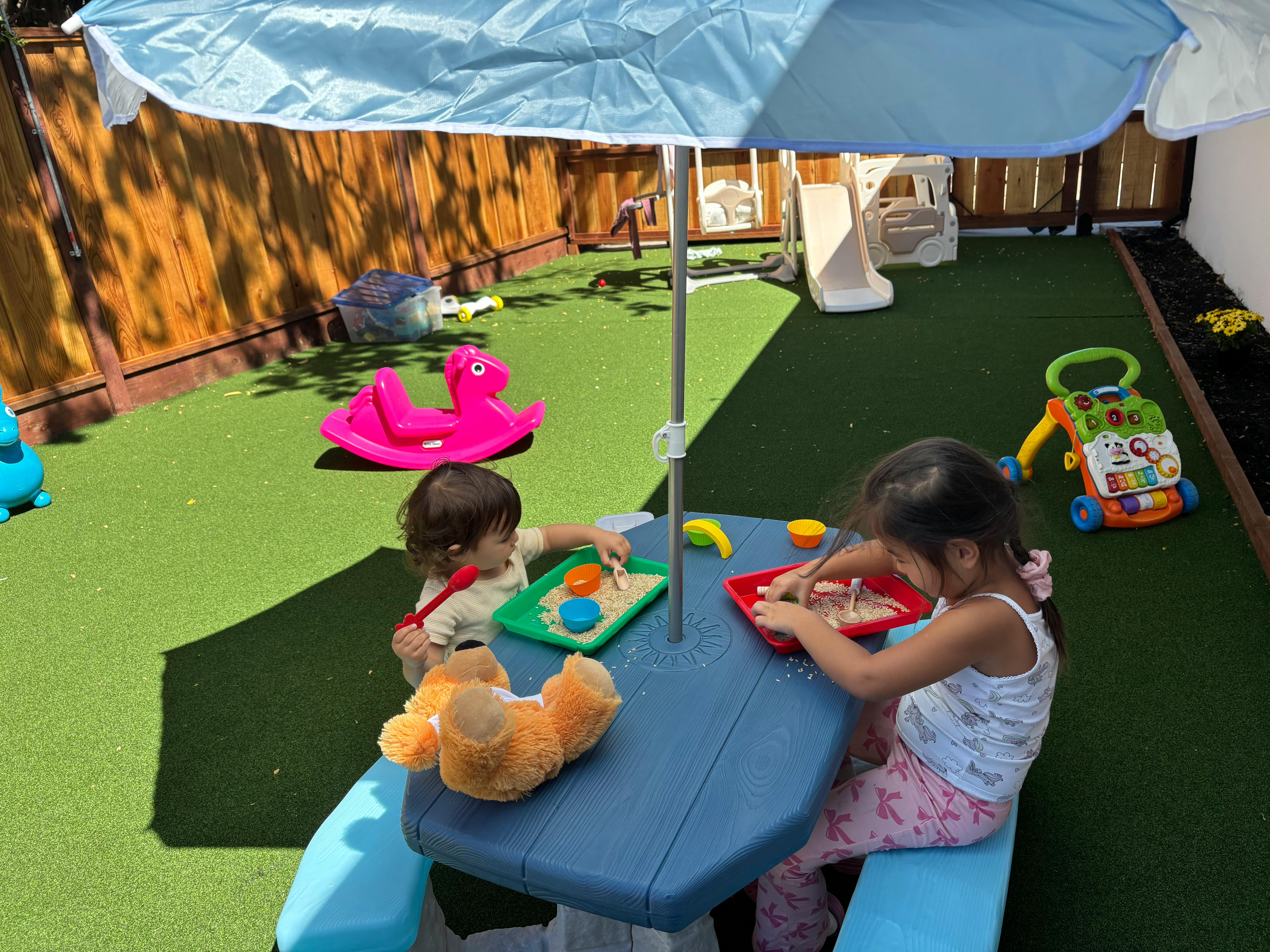 Two children playing at a blue picnic table under an umbrella