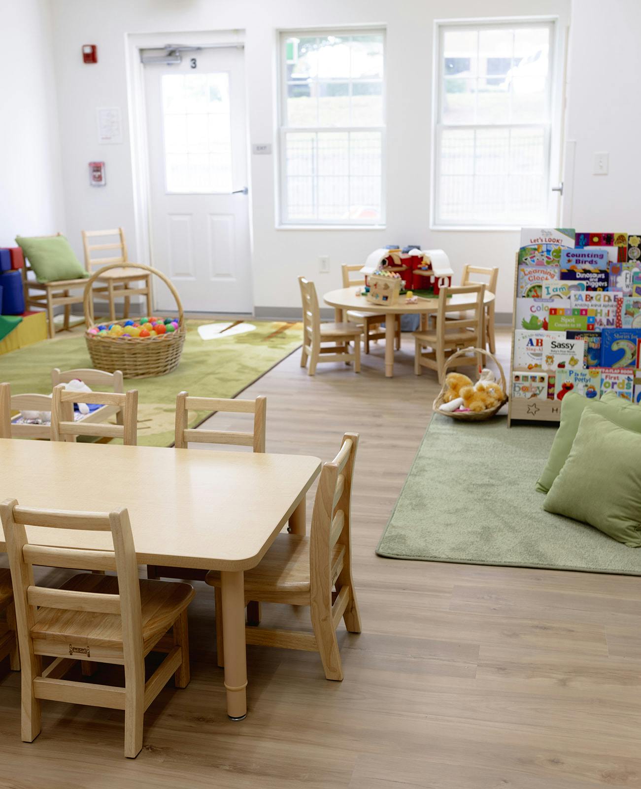 Classroom with small tables and chairs, green rugs, and a book display