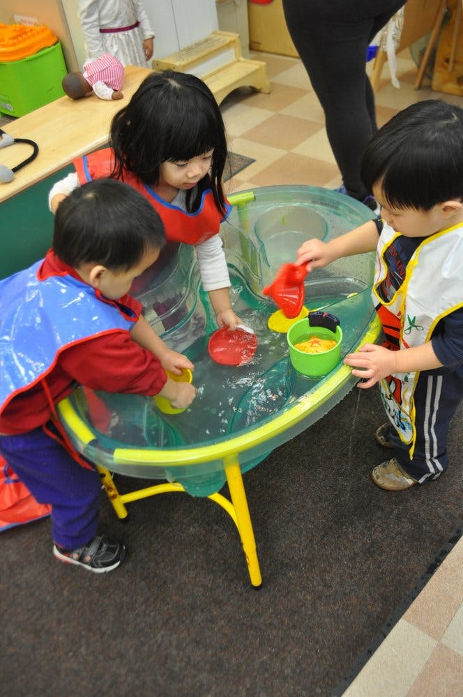 Three children playing with water and toys in a water table