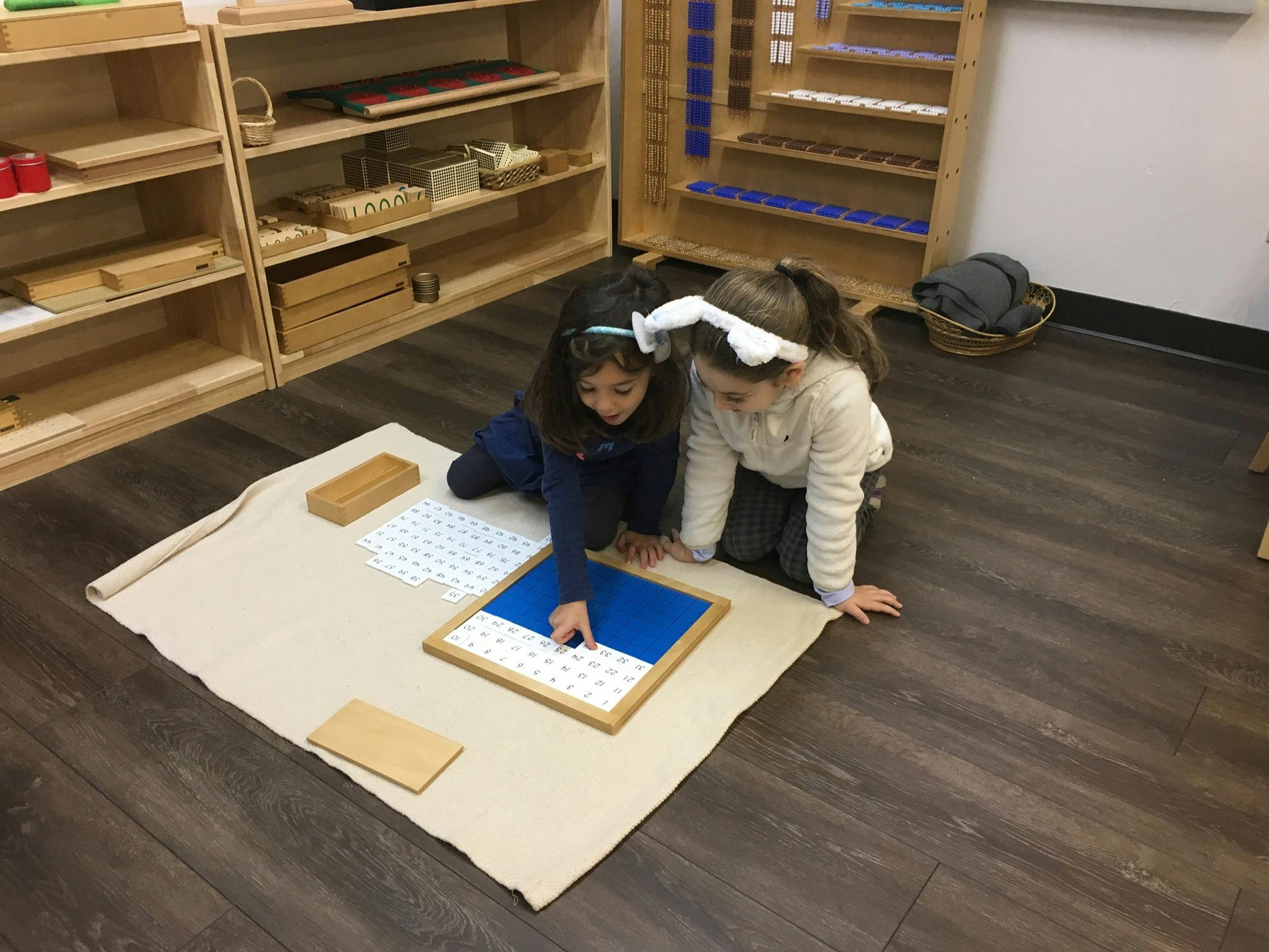 Two children kneeling on floor, interacting with a learning board