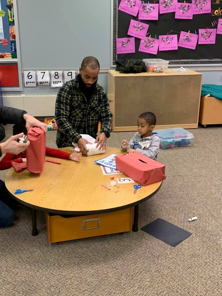 Adults and child at a table wrapping items in a classroom
