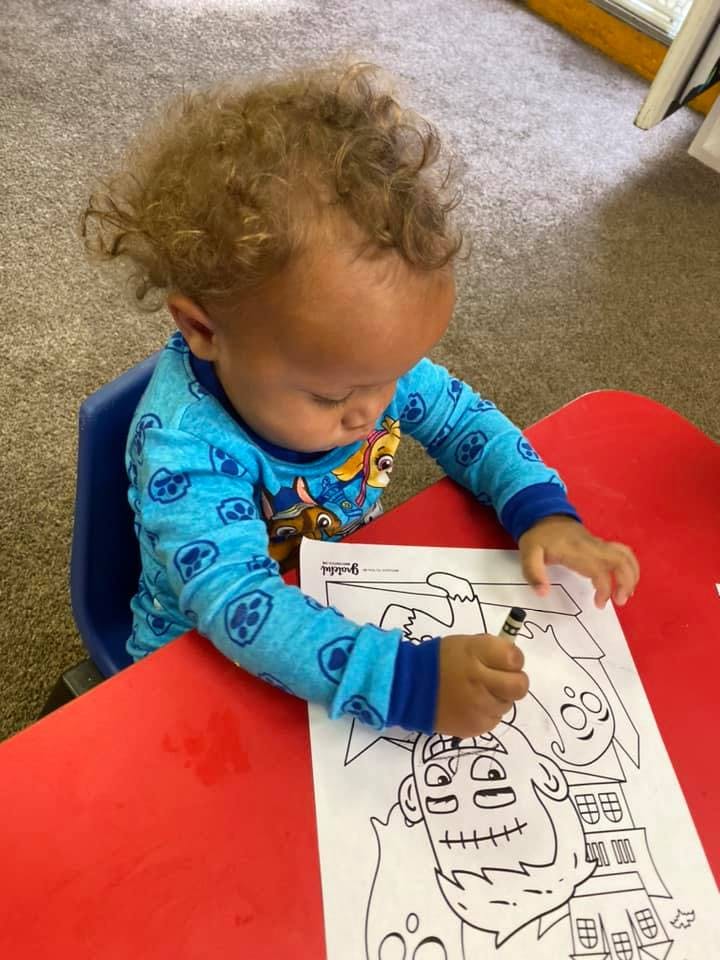 Child coloring a picture of a monster and ghost at a table