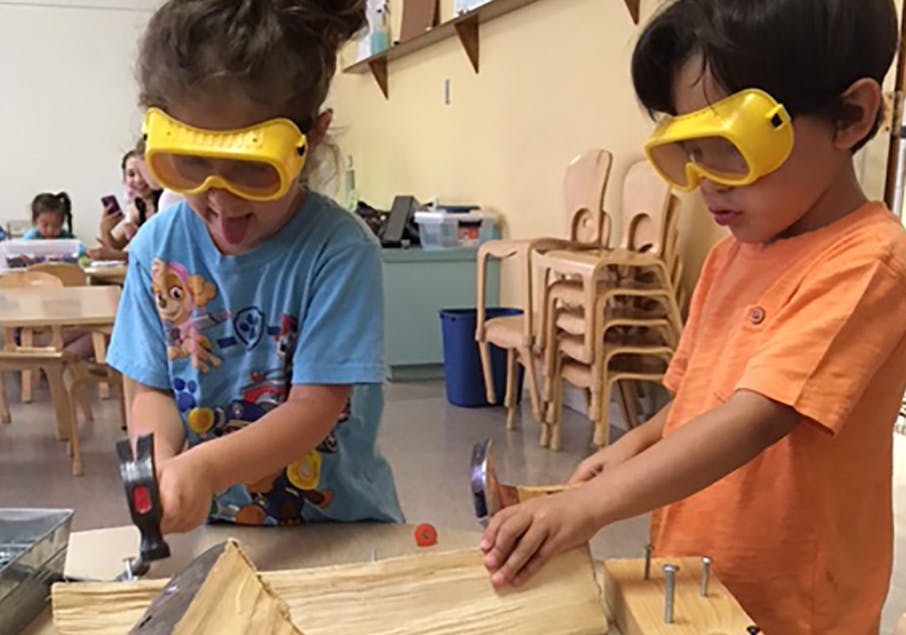 Two children wearing safety goggles hammering nails into wood