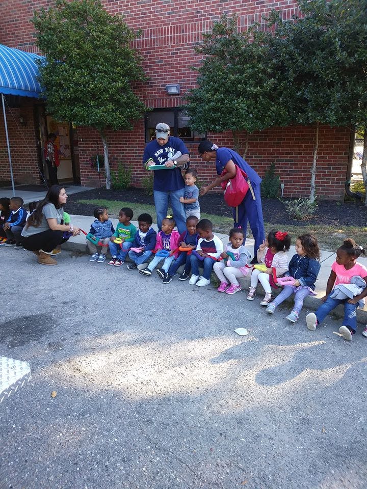 Adults interacting with a group of children sitting on the ground outdoors