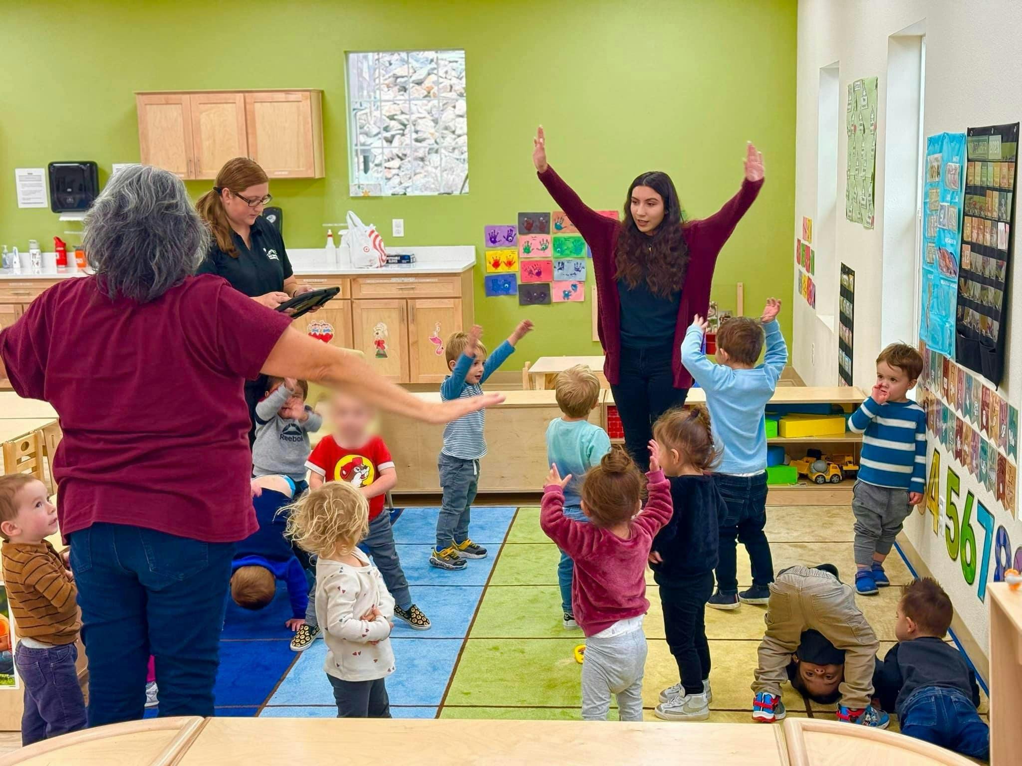 Adults and children in a classroom, some with arms raised