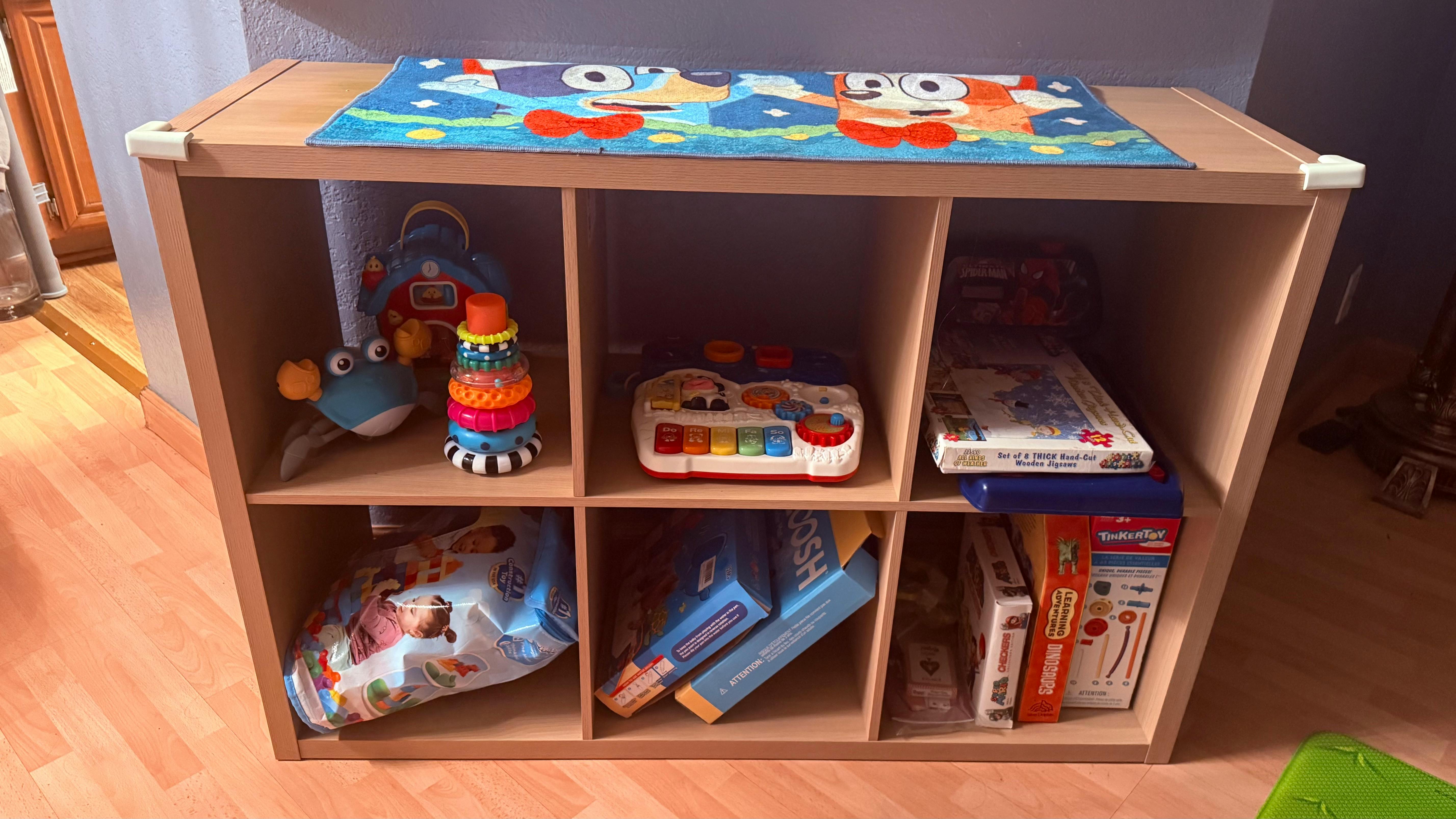 Wooden toy shelf with six compartments holding a variety of children's toys