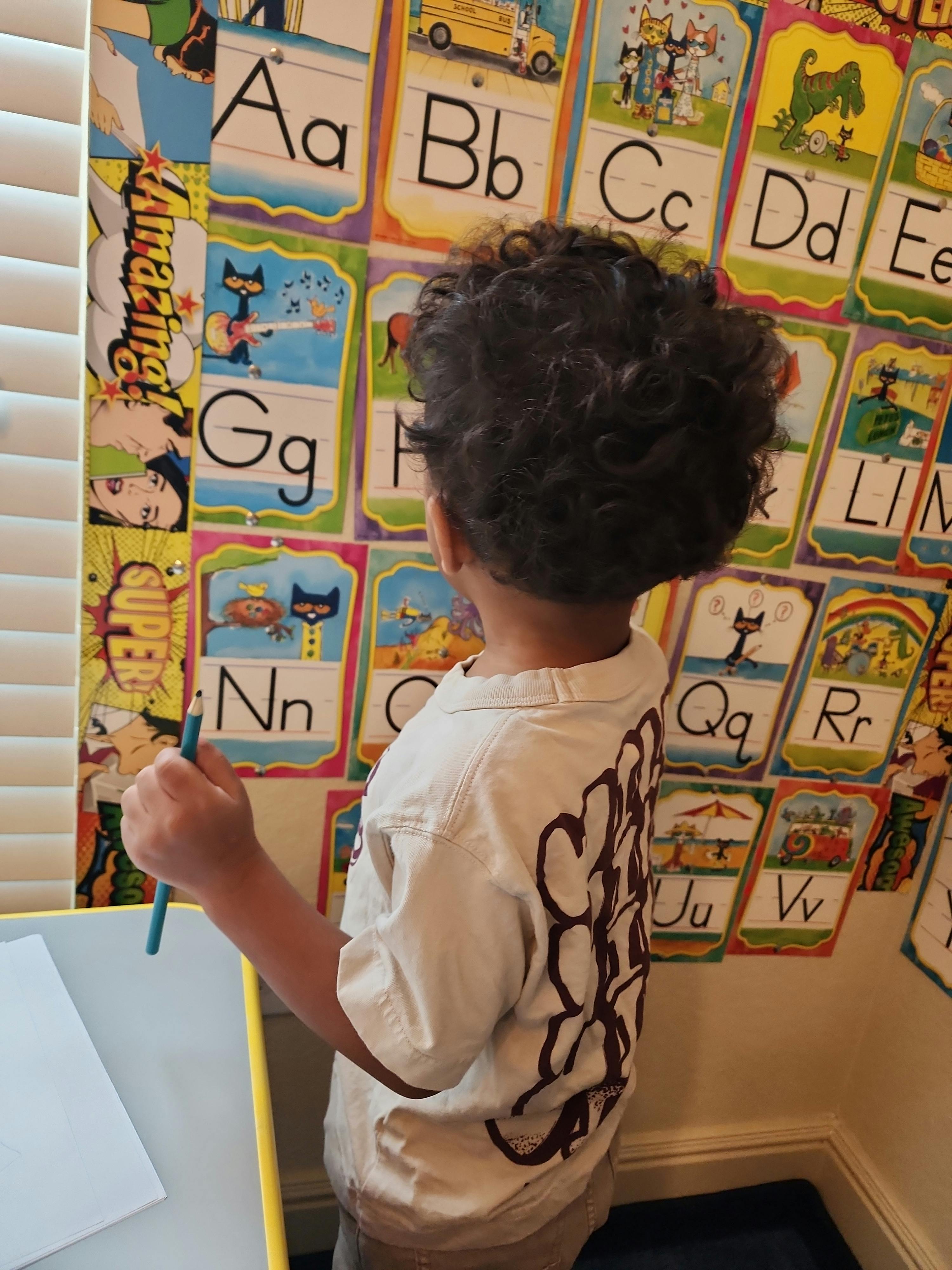 Child holding a pencil in front of alphabet posters