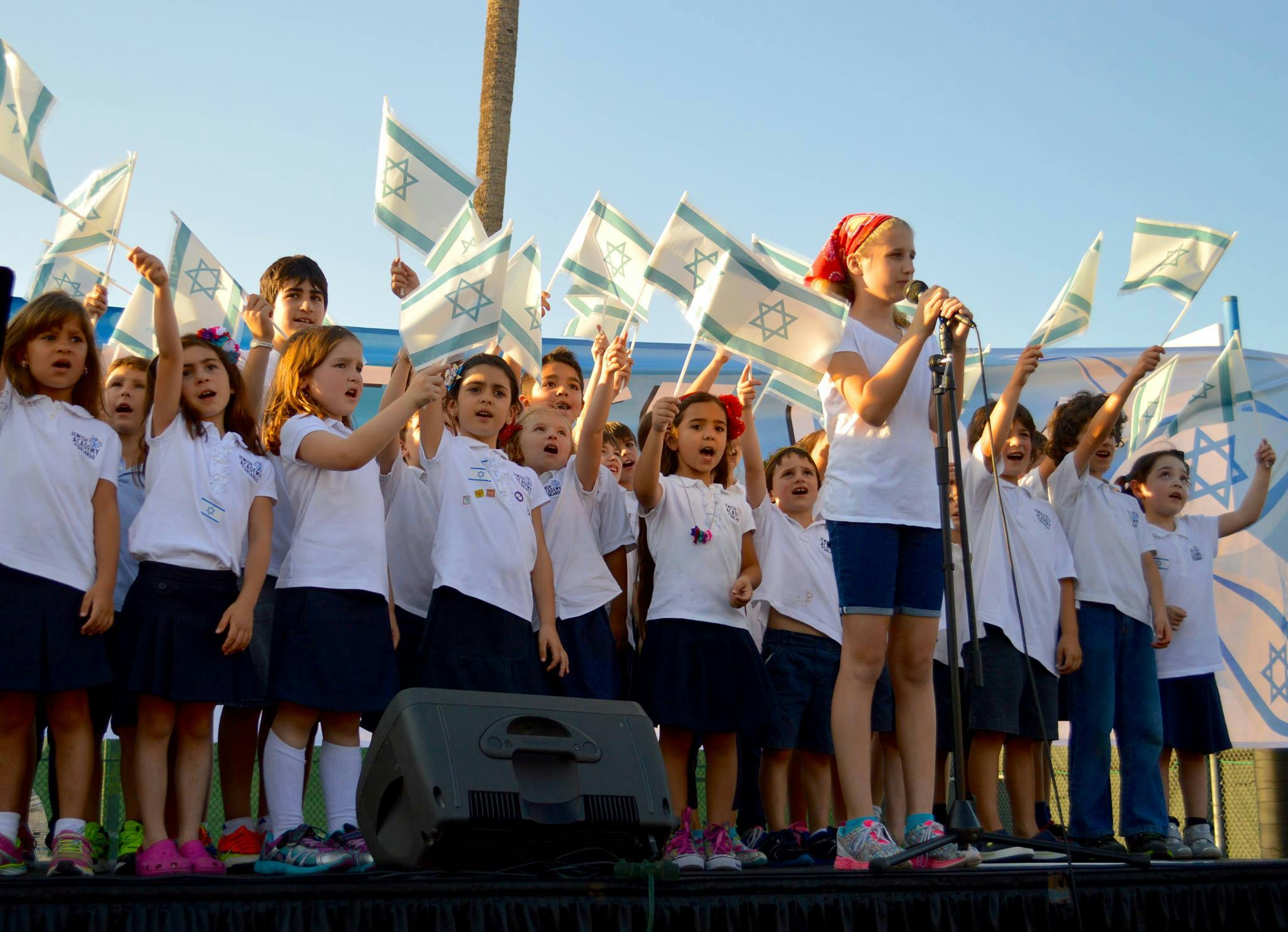 Children on a stage holding flags, one teen singing into a microphone