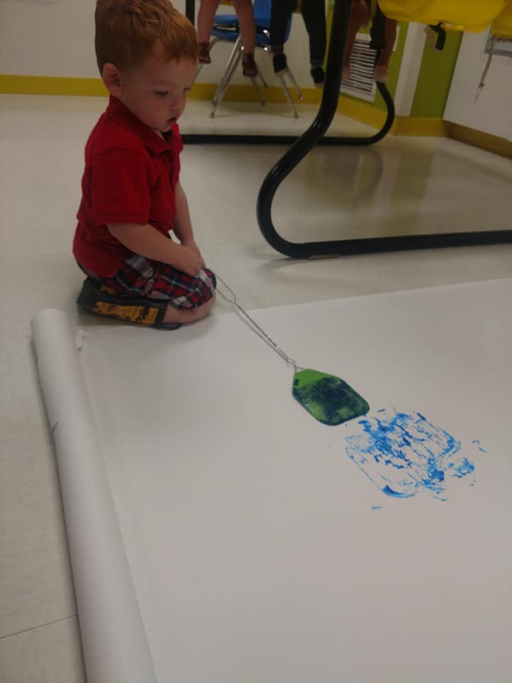 Child kneeling on floor painting with a tool on large paper