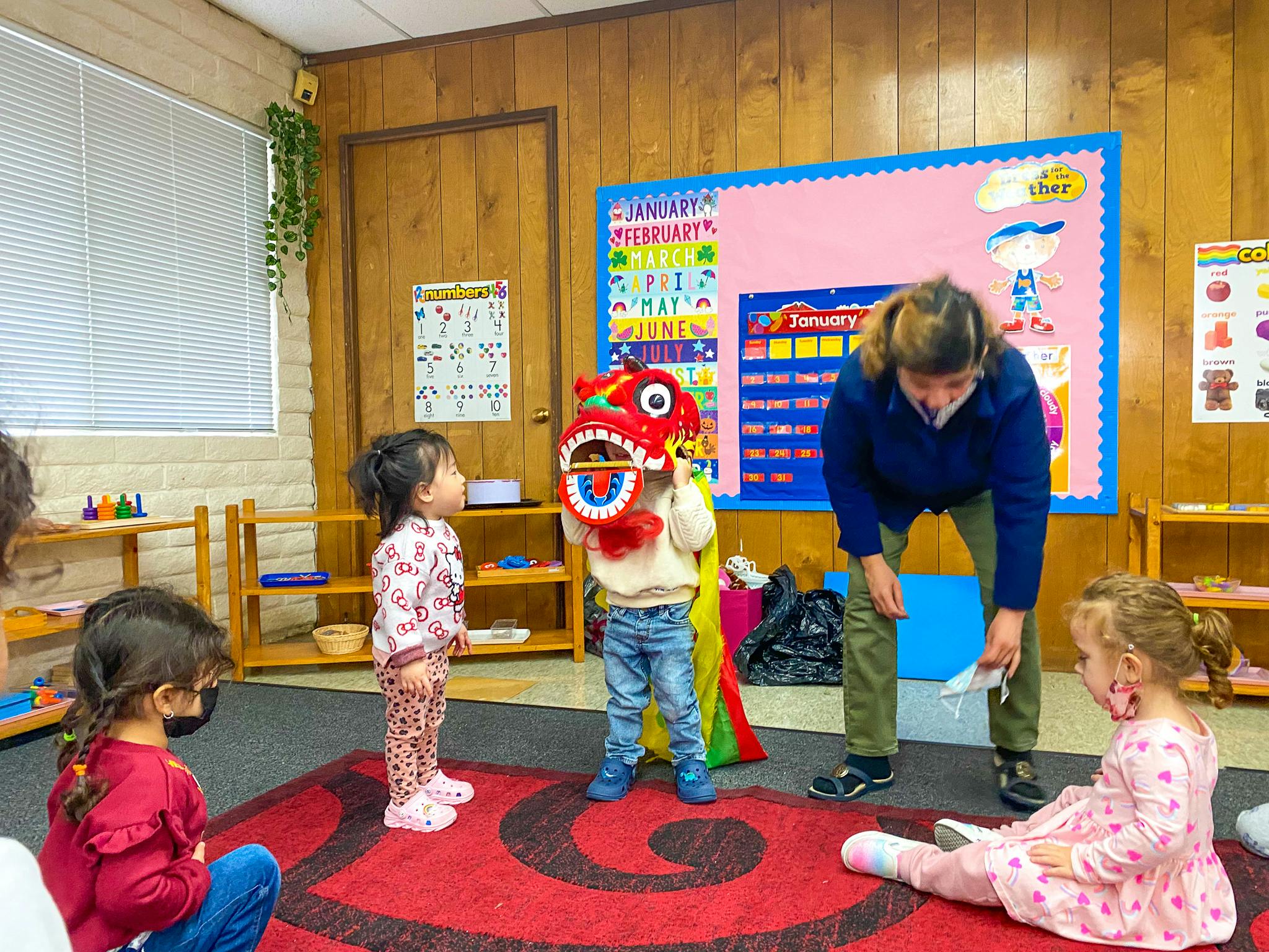 Adult and children in a classroom, one child holding a red dragon head
