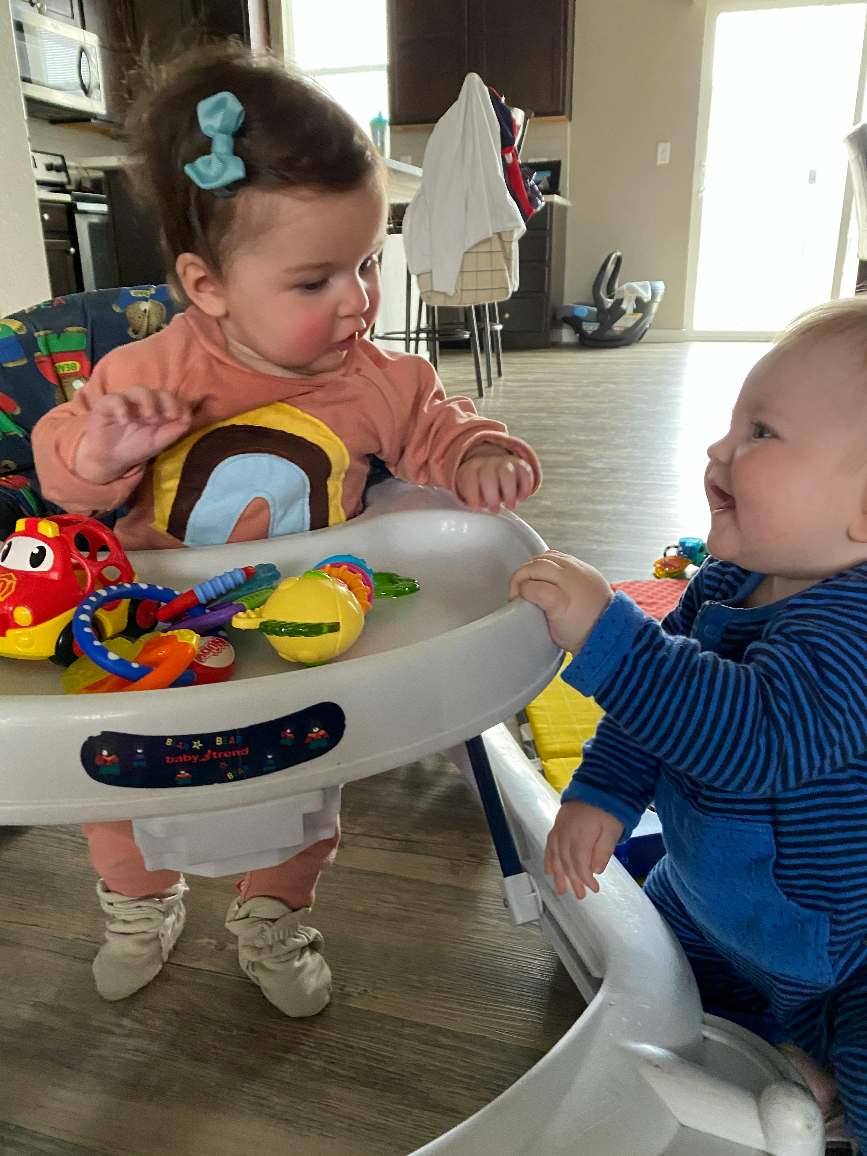 Two children playing with toys in a high chair and a baby bouncer